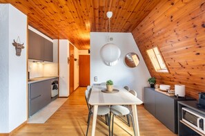 Une cuisine moderne avec un plafond en bois, un coin repas avec une table blanche et une petite table à manger avec des chaises.