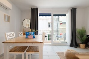En matplats med ett träbord och stolar, en krukväxt och utsikt genom en glasdörr till en balkong utomhus.