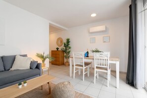 A modern living room with a sofa, a dining table with chairs, a wooden cabinet, and a small plant. - Cute Apt 50m from beach | Bonaire by PG (Sitges)