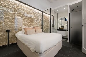 Ein modernes Schlafzimmer mit Steinsandsteinwand, einem Bett mit weißen Bettwäsche, einem Badezimmer mit Waschbecken und Spiegel sowie einer Tür.