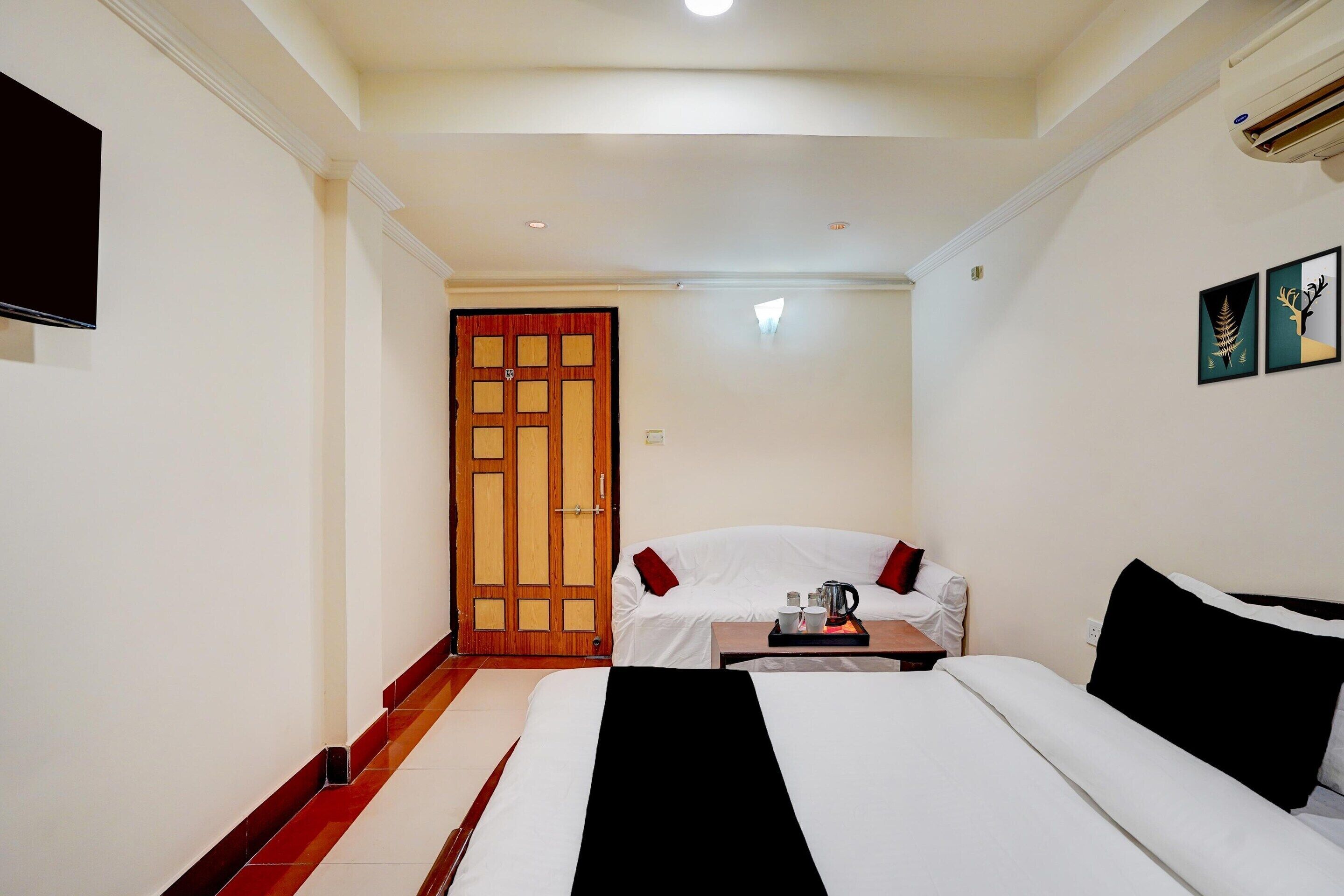 A hotel room with a bed, a sofa, a small table with a tray, a wooden door, and a wall-mounted TV.