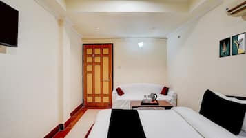 A hotel room with a bed, a sofa, a small table with a tray, a wooden door, and a wall-mounted TV.
