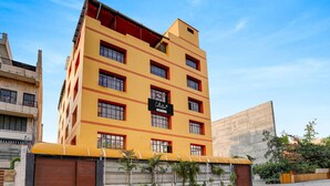 A multi-story building with a yellow facade, large windows, and a sign indicating a collection point. - Deluxe Banshi Bhawan (Prayagraj)