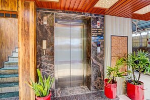 A hotel lobby with a marble wall, an elevator, and red potted plants. - Deluxe Banshi Bhawan (Prayagraj)