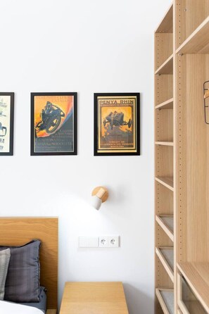 Ein Zimmer mit einem Bett, einem Nachttisch, einer Lampe und einem an der Wand befestigten Regal.