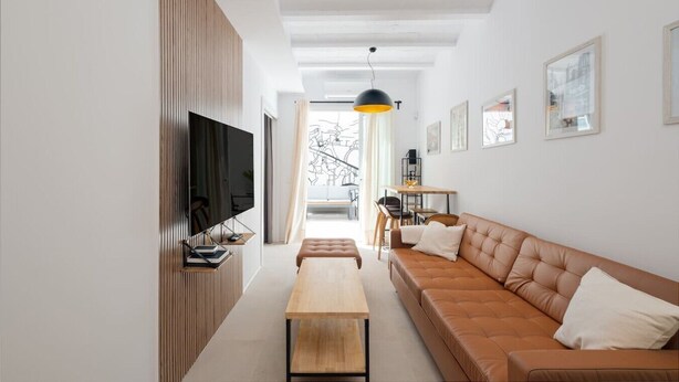 Un salon moderne avec un canapé, un téléviseur, un mur recouvert de panneaux en bois et un coin repas.