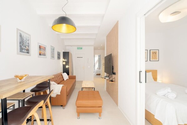 Ein modernes Hotelzimmer mit einer Couch, einem Esstisch, einem Hocker, einem Fernseher und einem Bett.