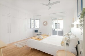 A bedroom with a bed, a desk, a chair, a ceiling fan, and a window. - Cute Apartment in the Heart of Vilanova | Virgi By Palmera (Vilanova i la Geltrú)