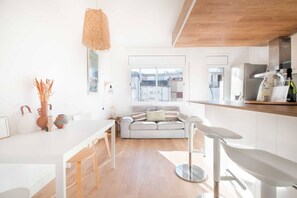 A modern kitchen with a dining area, a sofa, and a large window with a city view. - Cute Apartment in the Heart of Vilanova | Virgi By Palmera (Vilanova i la Geltrú)