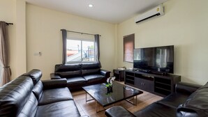 Ein Wohnzimmer mit schwarzem Ledersofa, einem Glastisch, einem Flachbildfernseher und einem Fenster mit Vorhängen.