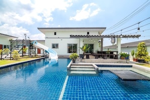 A swimming pool with a slide, a patio area, and a building with a tiled roof.