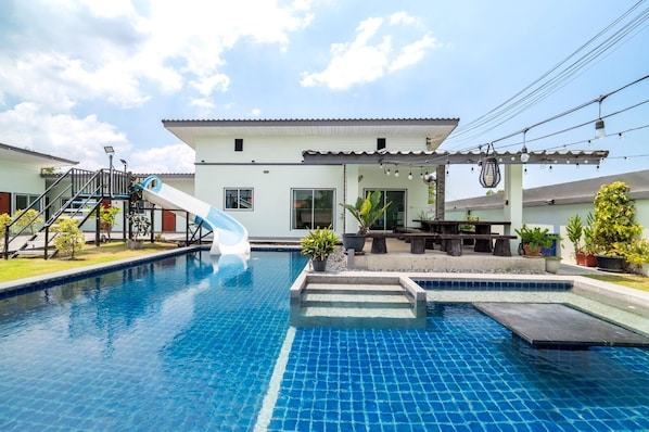A swimming pool with a slide, a patio area, and a building with a tiled roof. - Room-blue Lake Residences Pattaya - 2 BR (Bang Lamung)