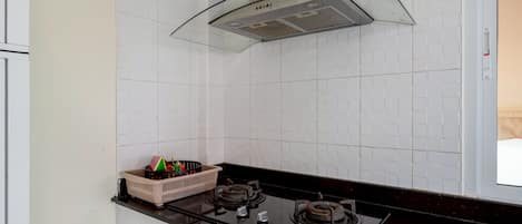A kitchen with white tiled walls, a black countertop, a gas stove, and a basket of fruits.