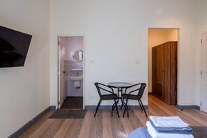 A modern room with a wooden floor, a round table with two chairs, a TV mounted on the wall, and a wooden door leading to another room.