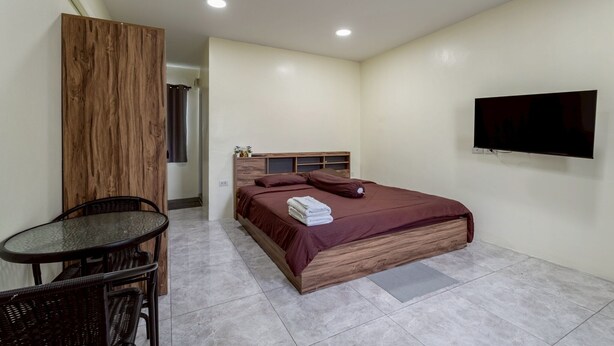 Ein Hotelzimmer mit Bett, einem an der Wand montierten Fernseher, einem kleinen Tisch mit Stühlen und einer Klimaanlage.