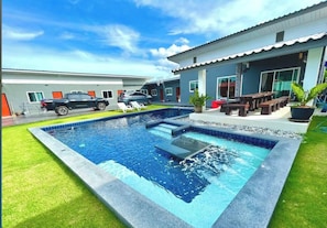 A swimming pool with a tiled edge, surrounded by a well-maintained lawn, and a building with a flat roof and large windows. - Room-blue Lake Residences Pattaya - 2 BR (Bang Lamung)