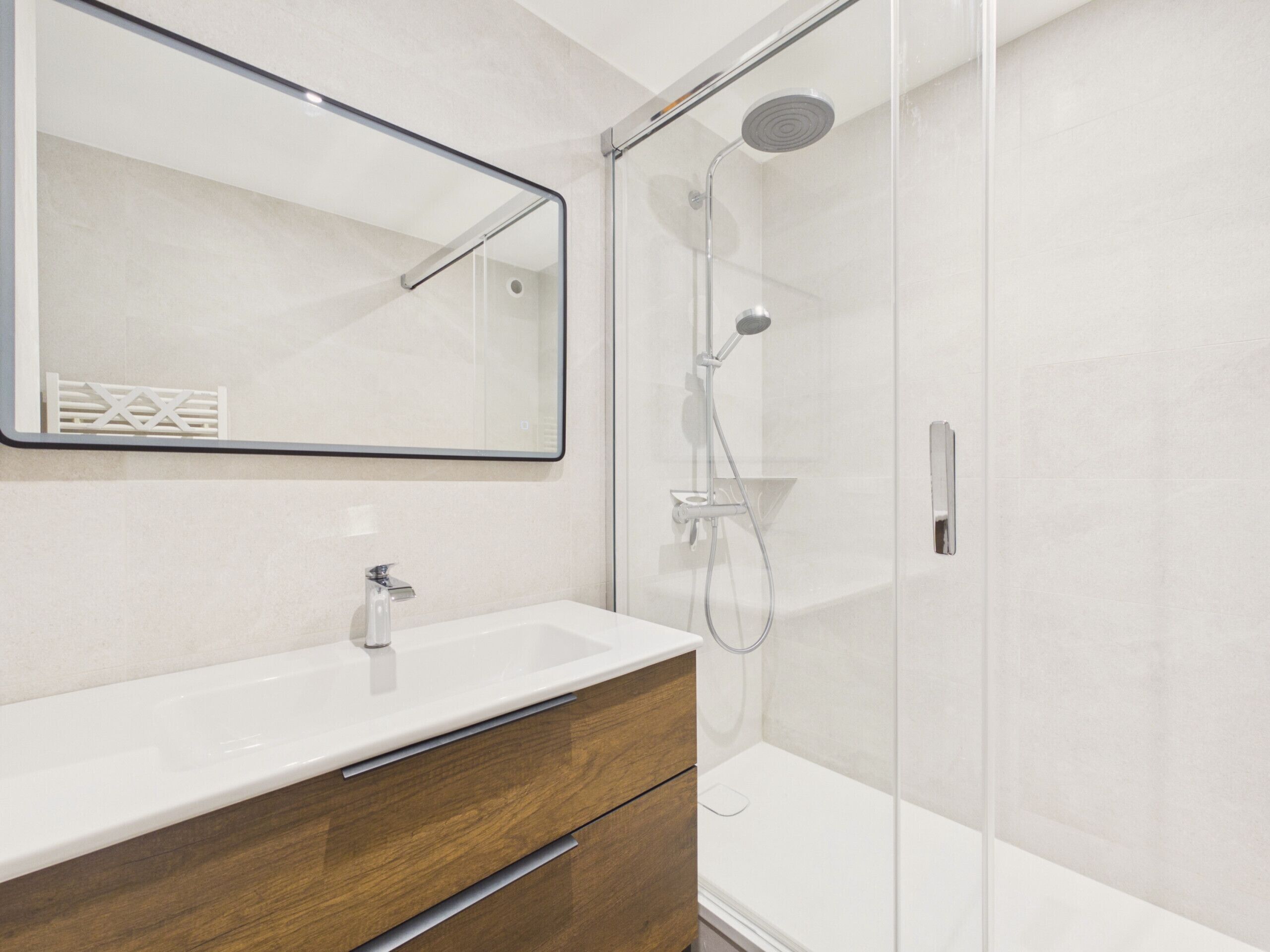 A modern bathroom with a glass shower enclosure, a white sink, and a wooden vanity.