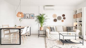 Un salon moderne comprenant un coin repas, un ensemble de canapés, une table basse, un luminaire suspendu, une plante en pot et des éléments de décoration murale.