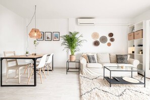 A modern living room with a dining area, a sofa set, a coffee table, a hanging light fixture, a potted plant, and wall decor. - Sunny & Stylish Apartment with A/C | Trini by Palmera (Sant Pere de Ribes)