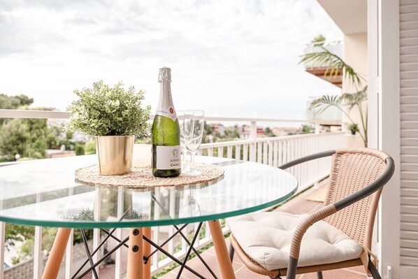 A glass table with a bottle and glass on it, a wicker chair, and a potted plant. - Sunny & Stylish Apartment with A/C | Trini by Palmera (Sant Pere de Ribes)
