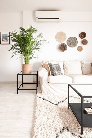 A modern living room with a white sofa, a black coffee table, a potted plant, and a wall-mounted air conditioner. - Sunny & Stylish Apartment with A/C | Trini by Palmera (Sant Pere de Ribes)