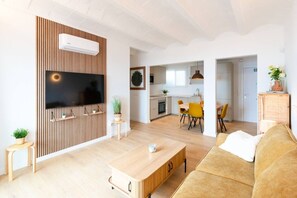 A modern living room with a flat-screen TV, wooden panel wall, and a dining area with yellow chairs. - 100 m from the Beach - Downtown Sitges | Sebas by PG (Sitges)