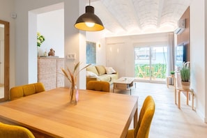 Ein modernes Wohnzimmer mit einem Holzesstisch, gelben Stühlen, einer Couch und einem Balkon mit Pflanzen.