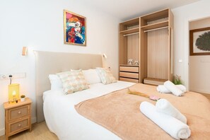 Ein Schlafzimmer mit Bett, Nachttisch, Lampe, Kunstwerk, Kleiderschrank und Handtüchern.