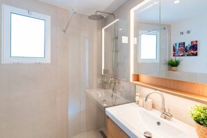 Ein modernes Badezimmer mit Duschkabine aus Glas, einem großen Spiegel und einem Waschbecken mit Holzschrank.