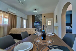Una habitación de hotel con una mesa de comedor para dos, una cama, un televisor y un equipo de aire acondicionado.