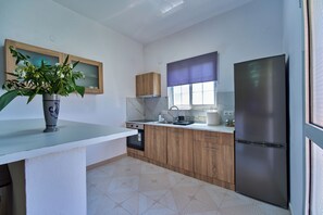 Une cuisine moderne dotée d’un four encastré, d’un réfrigérateur en acier inoxydable, de meubles en bois et d’une fenêtre avec un store violet.