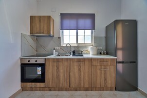 Una cocina con armarios de madera, un refrigerador de acero inoxidable, un ventanal con persiana y un horno empotrado.