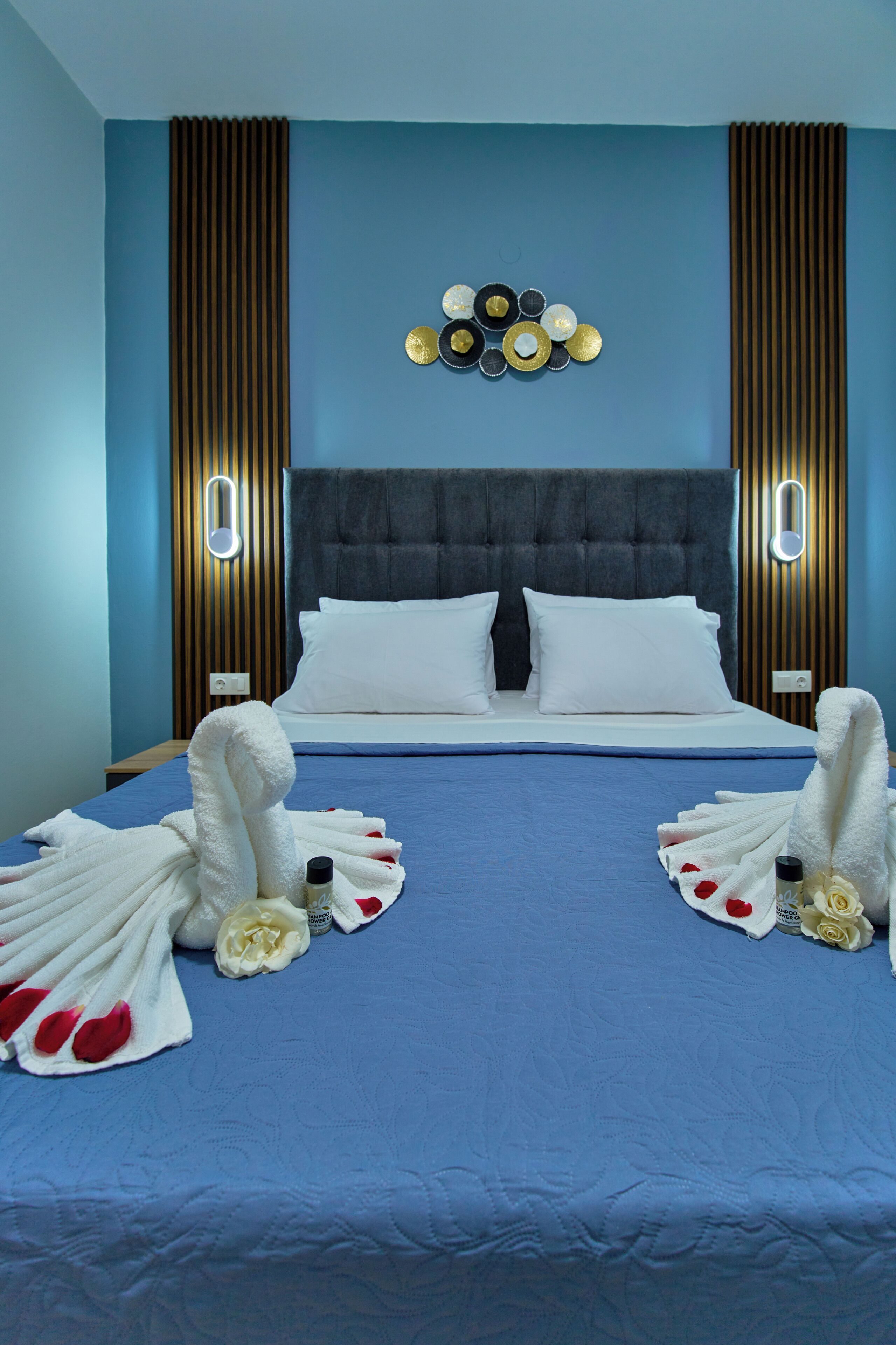 A hotel room with a blue bedspread, a tufted headboard, and a wall-mounted light fixture.
