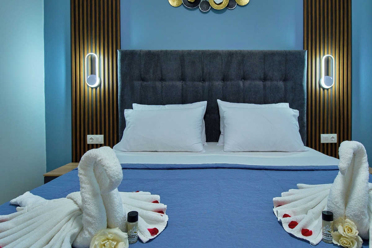 Habitación de hotel con colcha azul, cabecera capitonada y lámpara fijada a la pared.
