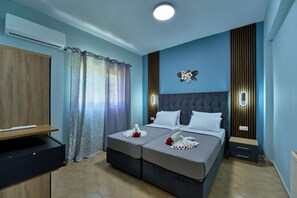 A double bed with a grey headboard, a bedside table, a wall-mounted light, and a decorative wall piece. - Villa Escapes By The Beach (Sidari)