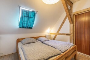 A bedroom with a sloped ceiling, a bed with patterned bedding, a nightstand, a window with curtains, and a wooden door.