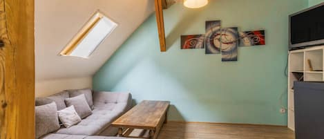 A loft-style room with a sloped ceiling, a sofa, a wooden table, a bench, and a TV on a stand.