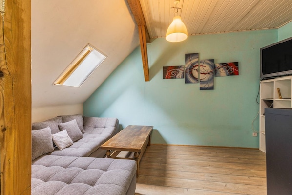 A loft-style room with a sloped ceiling, a sofa, a wooden table, a bench, and a TV on a stand.