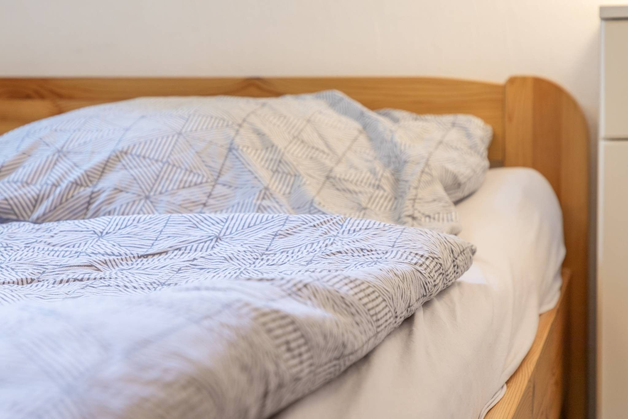 A bed with a patterned blanket and pillows, a wooden headboard, and a white wall.