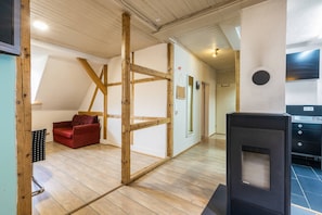 A room with exposed wooden beams, a red sofa, a black stove, and a door leading to another room.