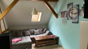 A loft-style room with a sectional sofa, a wooden coffee table, a hanging pendant light, and a skylight.