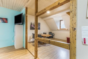A room with a wooden ceiling, a television, a dining table with chairs, and a window.