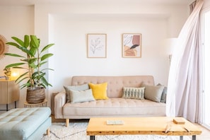 A living room with a sofa, a coffee table, a side table, and a potted plant.