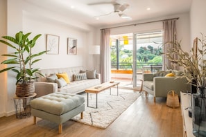 A modern living room with a sofa, armchair, and ottoman, a coffee table, and a large window with a view of greenery.