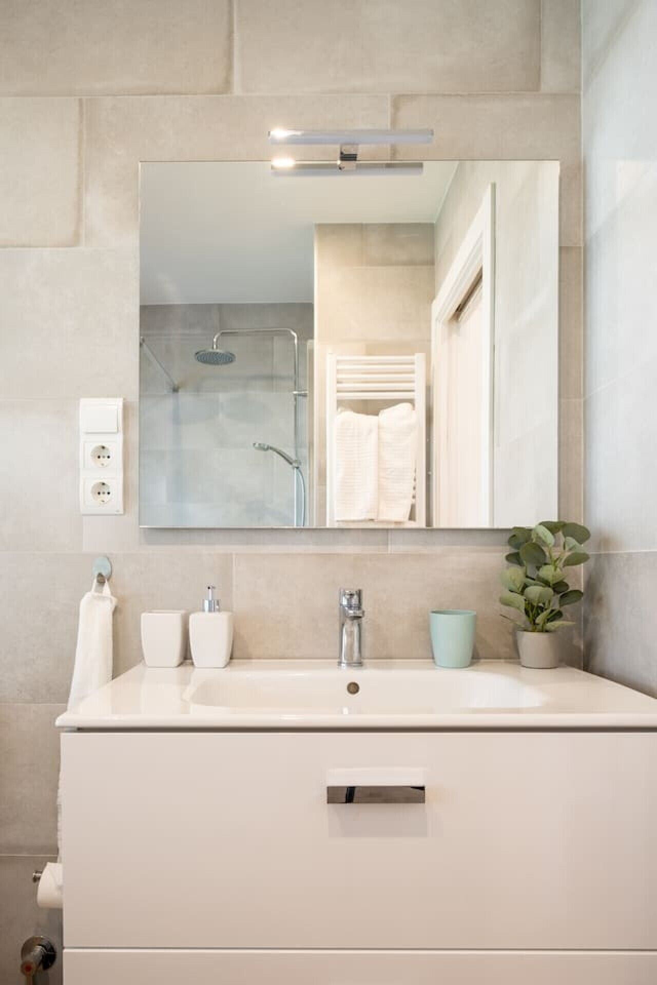 A bathroom with a large mirror, a sink, a shower, and a potted plant.