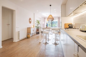 A modern kitchen with a central island, bar stools, and a hanging light fixture.