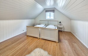 Un dormitorio con suelo de madera, una cama con cabecera, una mesita de noche, una lámpara y una ventana.