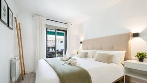 Une chambre d’hôtel avec un lit, une table de chevet ornée d’une plante, une fenêtre avec des rideaux et un radiateur.