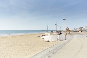 Una playa con un paseo marítimo, una gran escultura y un muelle al fondo.