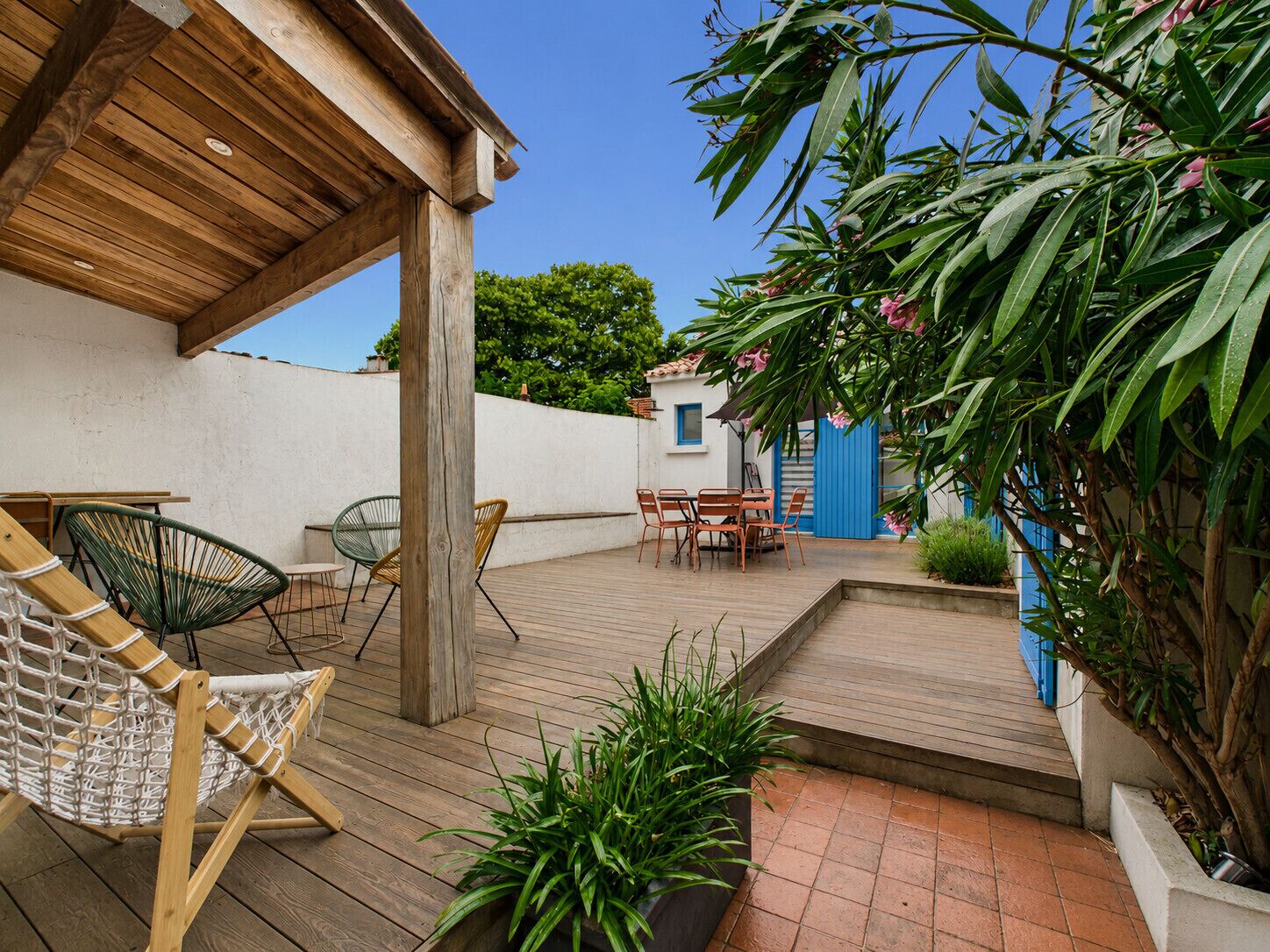 Um deck de madeira com móveis de exterior, uma cadeira suspensa e vasos com plantas.